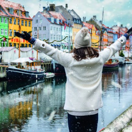 A happy tourist woman enjoys the view to the beautiful Nyhavn area in Copenhagen, Denmark, during winter time with snow and Christmas decorations