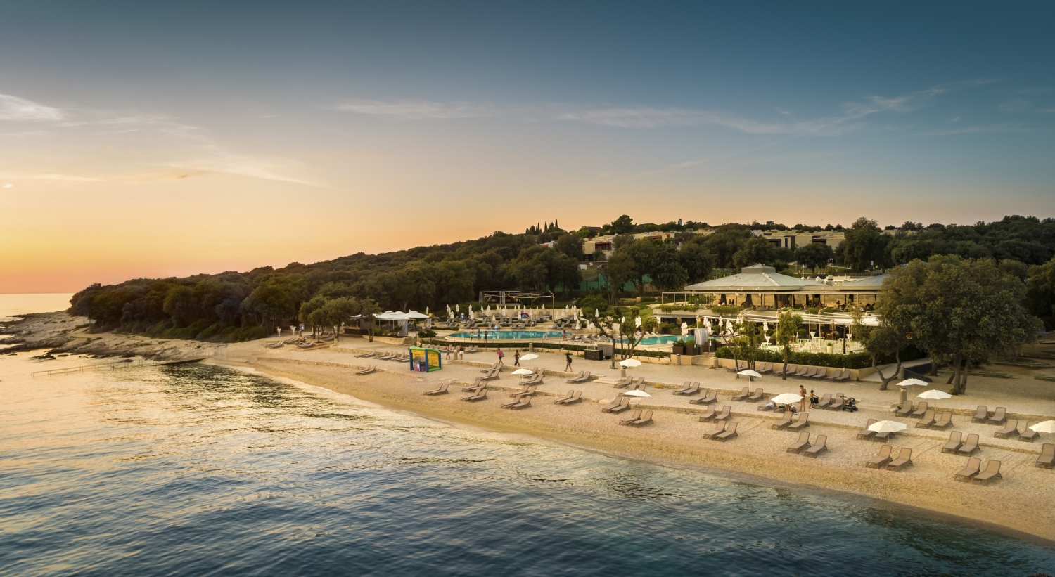 Strandresort mit Sonnenschirmen und Liegen am Wasser bei Sonnenuntergang