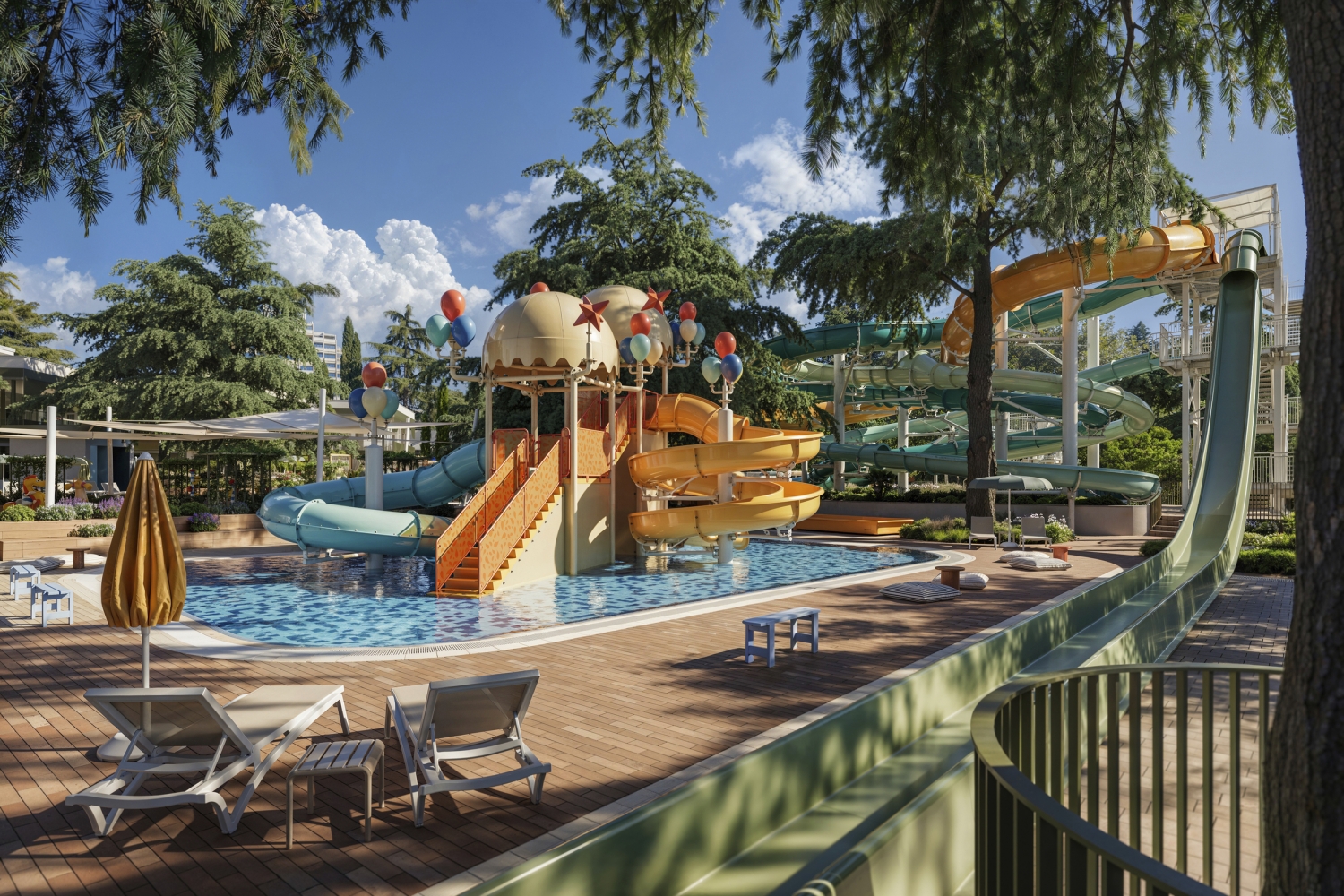 Wasserpark mit bunten Rutschen und Liegestühlen unter Bäumen bei sonnigem Wetter.