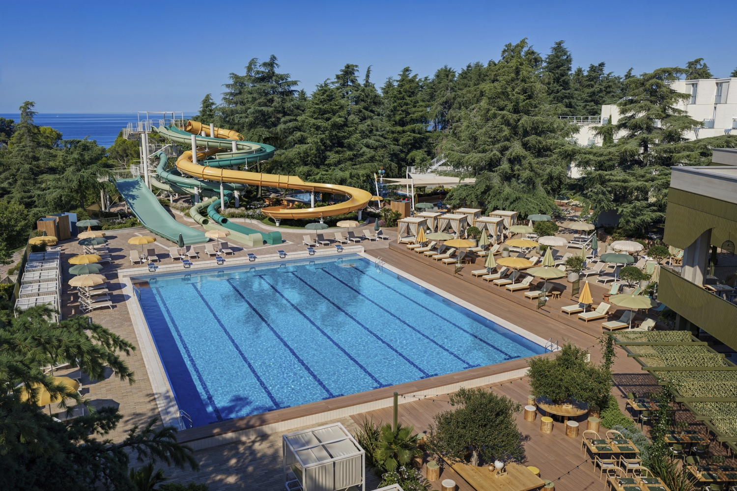 Außenansicht einer Ferienanlage mit Pool und Wasserrutsche in sonniger Umgebung.