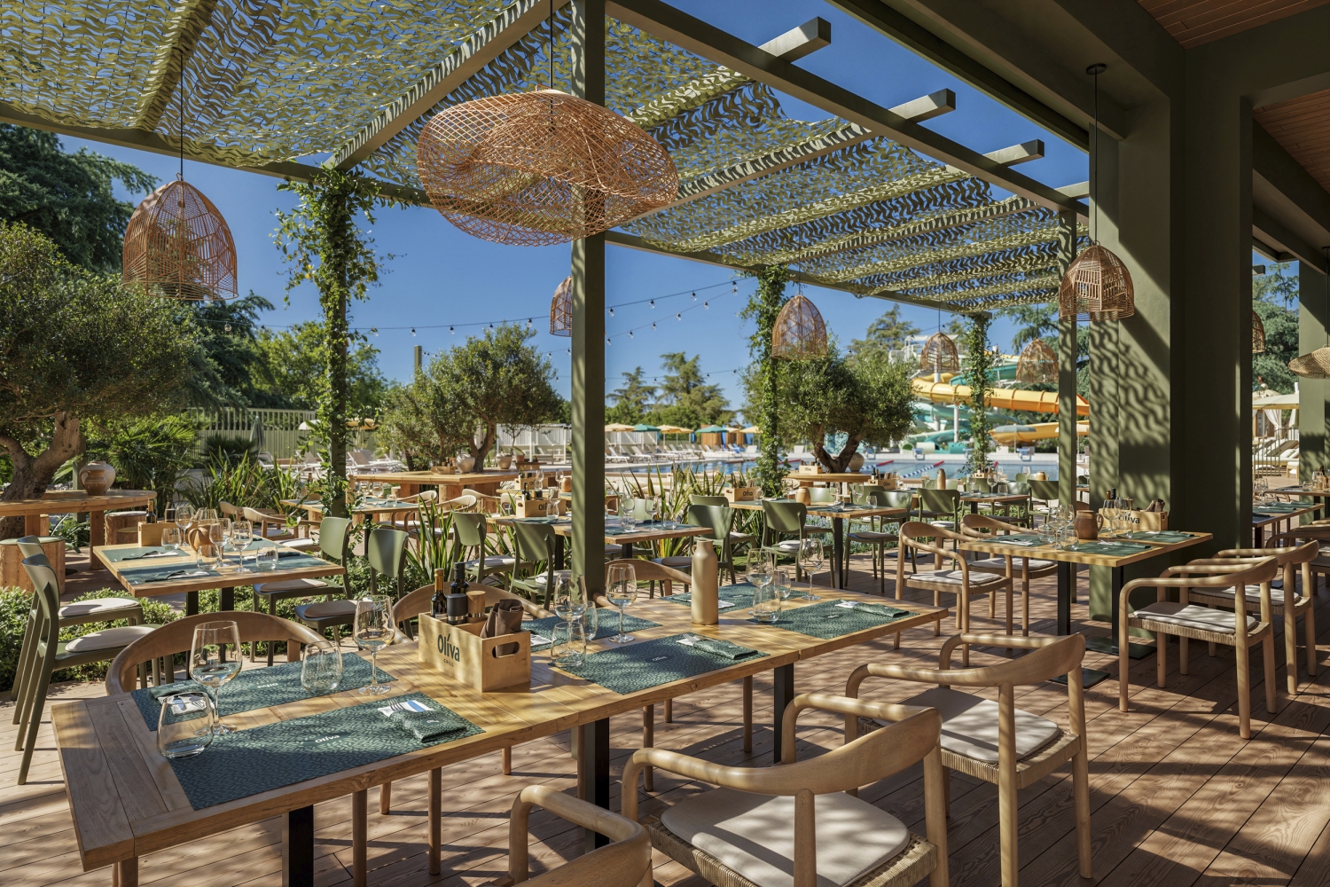 Restaurantterrasse mit gedeckten Tischen und Blick auf Poolbereich bei sonnigem Wetter.